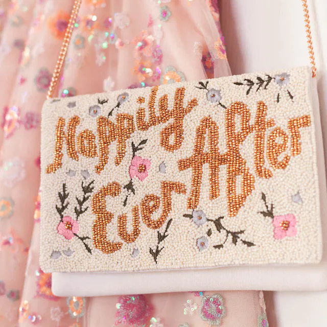 A beaded bridal clutch with 'Happily Ever After' text in gold, adorned with intricate floral patterns. Made from durable canvas, this 7 x 9.5 x 1 inch clutch showcases the unique charm of handmade items, ensuring no two are exactly alike. Ideal for holding wedding day essentials.