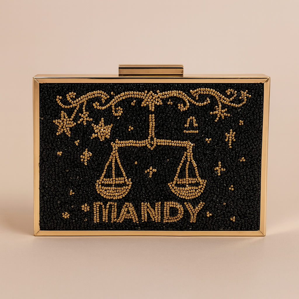 A rectangular clutch bag with a black background and gold embellishments, including a design of scales and stars.
