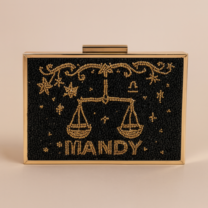 A rectangular clutch bag with a black background and gold embellishments, including a design of scales and stars.