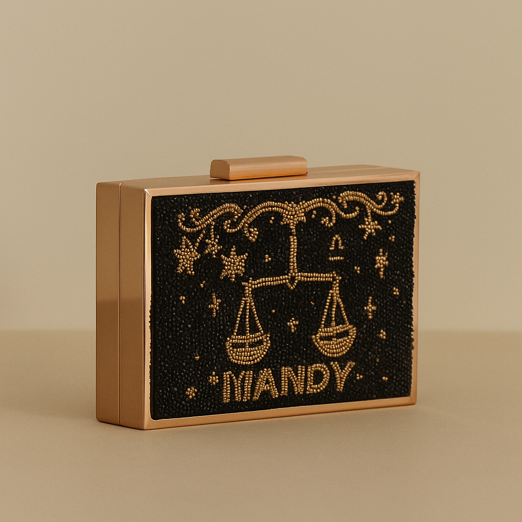 A rectangular, gold-colored clutch purse with a black, beaded design featuring a zodiac symbol and the word "IANDY" printed on it.