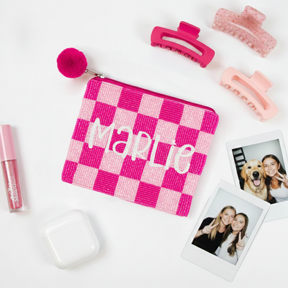a checkered pouch with the name "Marlee", a pair of pink hair clips, a white earbud, and two Polaroid photos of two smiling women.