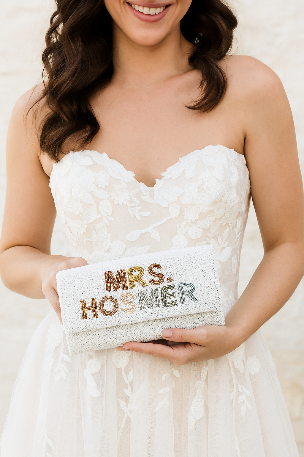 A woman in a white wedding dress holding a small clutch purse with the text "Mrs. Hosmer" printed on it.