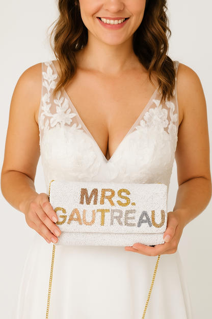 A woman in a white wedding dress holding a white clutch purse with the text "Mrs. Gautreau" printed on it.