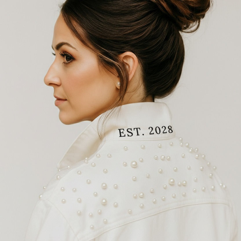 A woman with dark hair wearing a white jacket with a personalized embroidered text on the back.