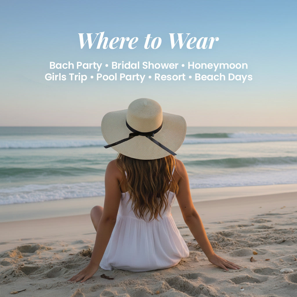 A woman in a white dress and wide-brimmed hat sits on a sandy beach, facing the ocean.