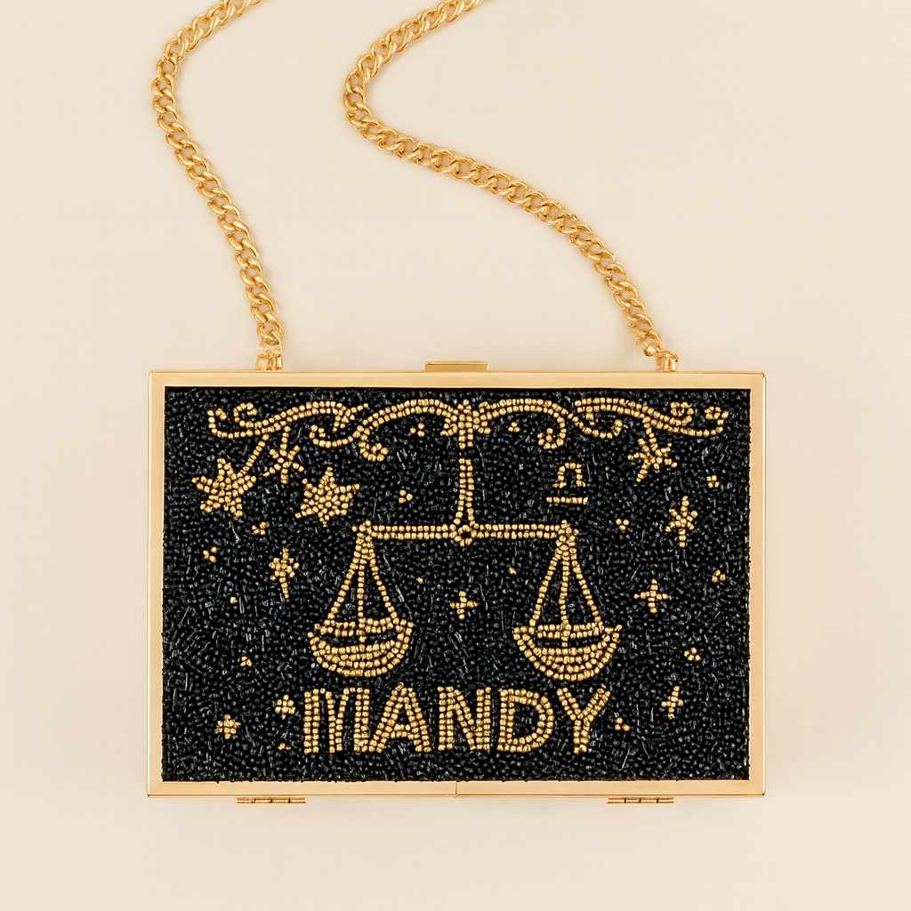 A handbag with a black background and gold embellishments, including a zodiac symbol and the word "MANDY" written on it.