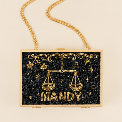 A handbag with a black background and gold embellishments, including a zodiac symbol and the word "MANDY" written on it.