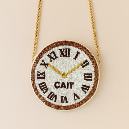 A round, beaded clock with Roman numerals and gold hands is suspended from a chain.