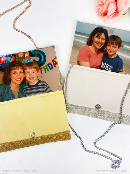 a purse with a chain strap, decorated with a photo of a woman and two children. The purse is placed on a white surface, and there is a pink flower in the background.