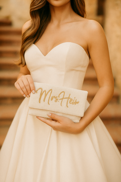A woman in a white wedding dress holds a small clutch purse with the name "Mrs. Hein" written on it.