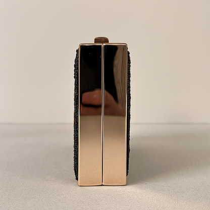 A shiny gold-colored clutch purse with a black woven strap.