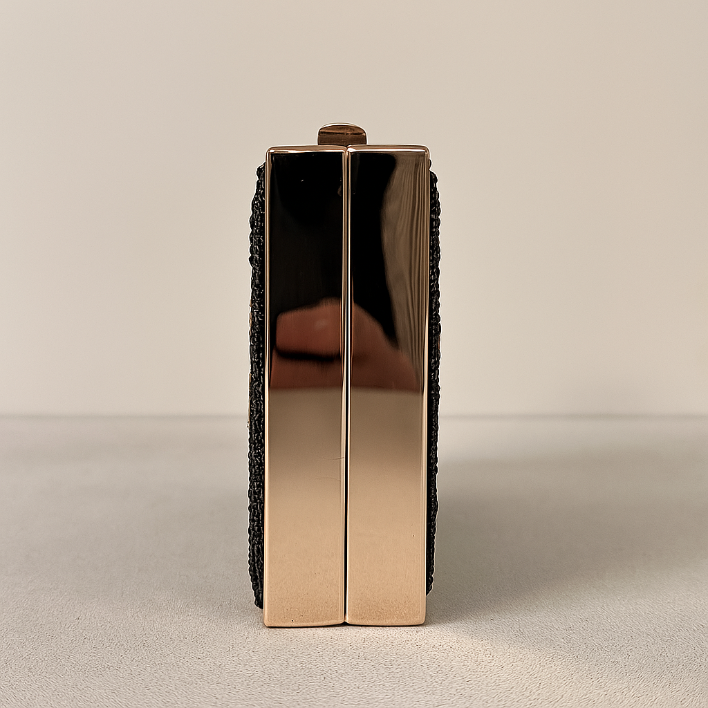 A shiny gold-colored clutch purse with a black woven strap.