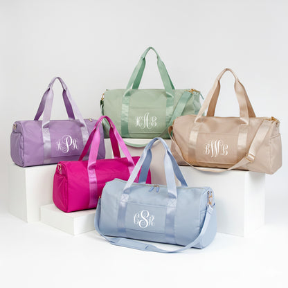a collection of five colorful duffel bags, each with a monogrammed initials printed on them.