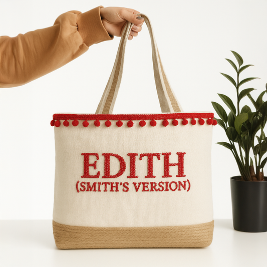 A hand holding a beige tote bag with red trim and the text "EDITH (SMITH'S VERSION)" printed on it.
