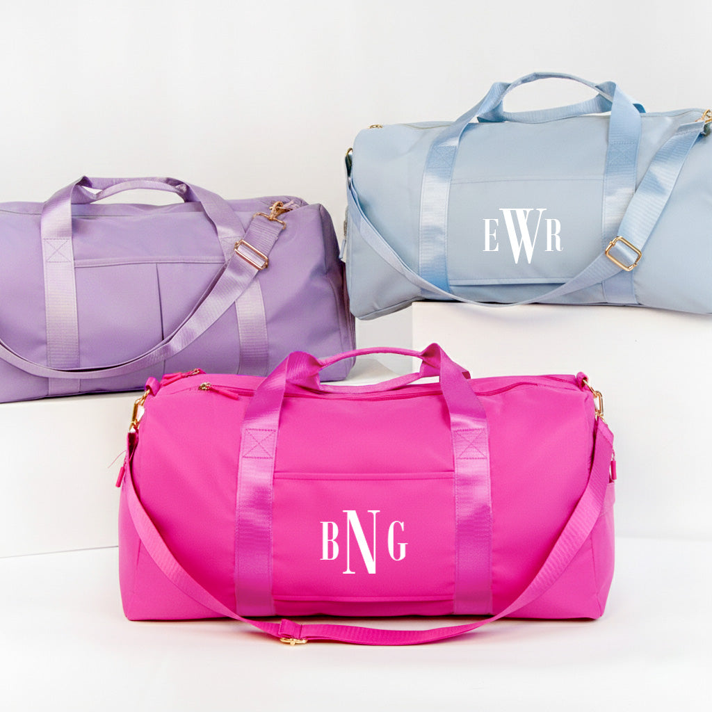 three colorful duffel bags, each with a unique color and monogram. The bags are arranged in a row, showcasing their vibrant designs and personalized monogrammed initials.