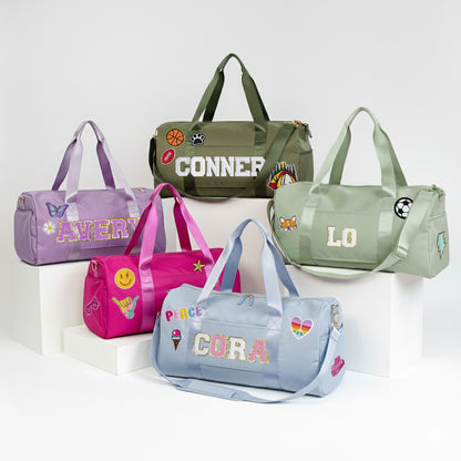 A collection of colorful duffle bags with various personalization details, including names and stickers, displayed on a white background.