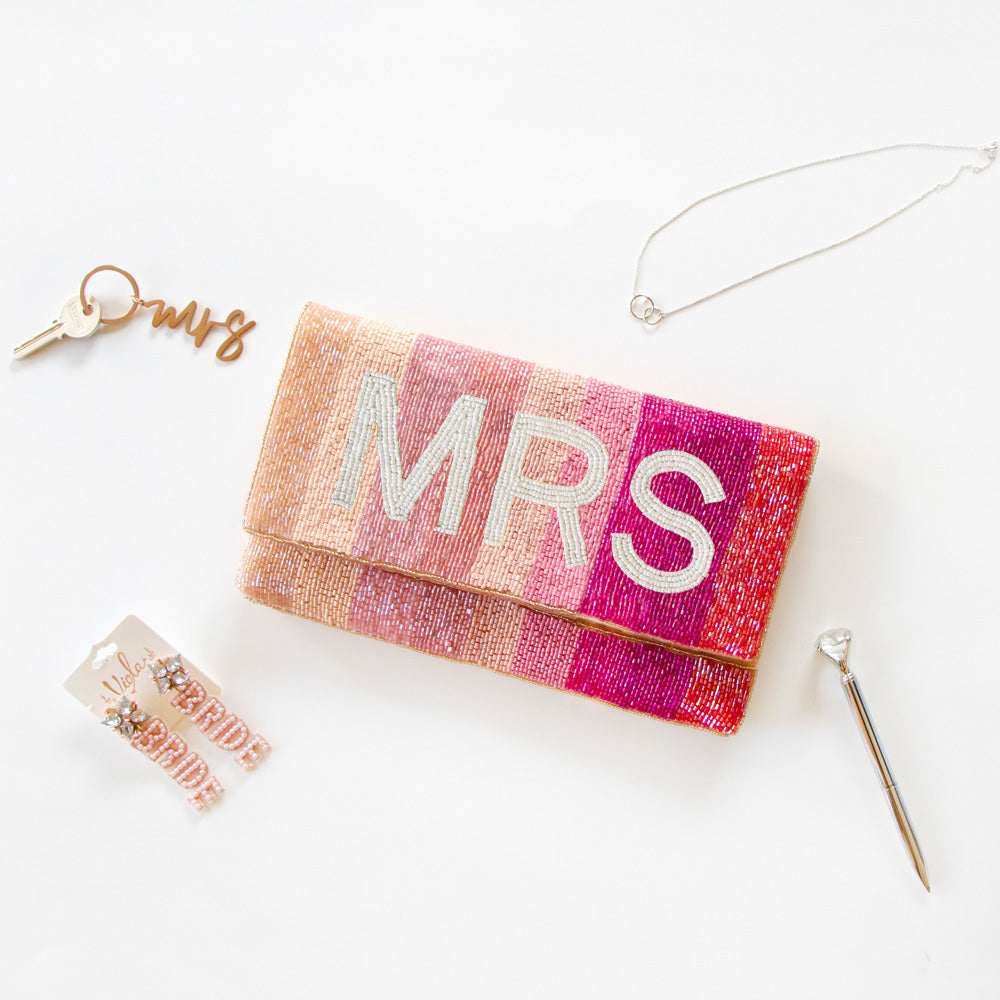 Exquisite Personalized Pink Ombre Clutch Bag, masterfully handcrafted for wedding occasions. Measuring 9.5 inches in length and 6 inches in breadth, this clutch features a gradient of pink hues, accented with white text beading. Complete with a gold or silver chain and plush velvet interior, it can be personalized with a date inside. A perfect blend of elegance and functionality, it's a distinctive accessory that adds a touch of sophistication to bridal attire.