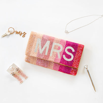 Exquisite Personalized Pink Ombre Clutch Bag, masterfully handcrafted for wedding occasions. Measuring 9.5 inches in length and 6 inches in breadth, this clutch features a gradient of pink hues, accented with white text beading. Complete with a gold or silver chain and plush velvet interior, it can be personalized with a date inside. A perfect blend of elegance and functionality, it's a distinctive accessory that adds a touch of sophistication to bridal attire.