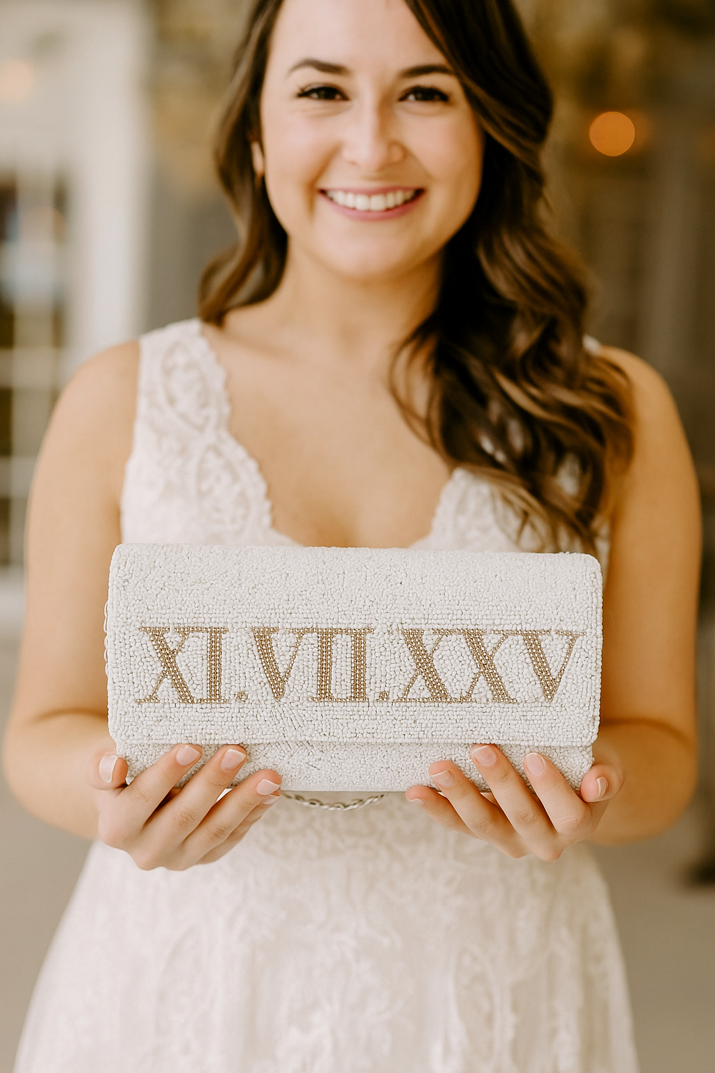 A smiling woman in a white dress holding a white clutch purse with the text "XII.VI.XXV" printed on it.