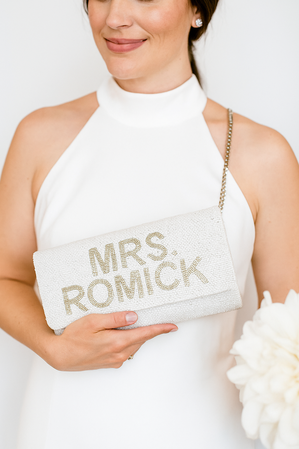 A woman in a white dress is holding a white clutch purse with the text "Mrs. Romick" printed on it.