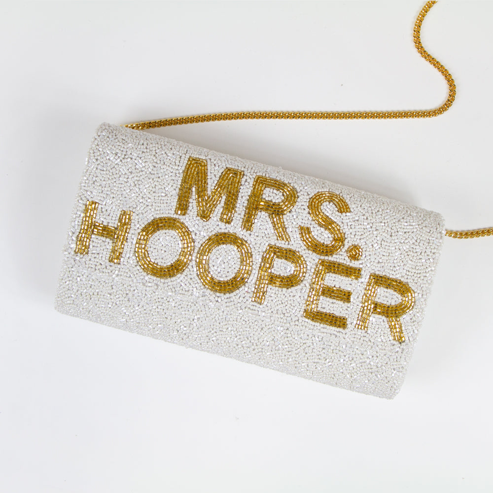 "Custom Mrs (Last Name)" beaded bridal clutch, intricately handmade for an elegant touch on the wedding day. Sized at 9.5in x 5in x 3in with an option for a gold or silver chain. Each bridal clutch boasts a unique character, highlighting the beauty of handcrafted items. Can be personalized with a custom date inside. An exquisite addition to any bridal ensemble or a thoughtful gift for soon-to-be brides.