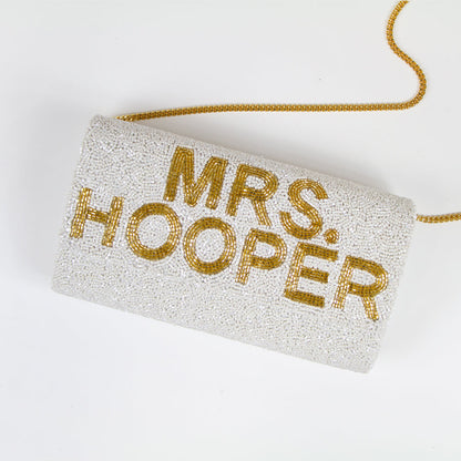 "Custom Mrs (Last Name)" beaded bridal clutch, intricately handmade for an elegant touch on the wedding day. Sized at 9.5in x 5in x 3in with an option for a gold or silver chain. Each bridal clutch boasts a unique character, highlighting the beauty of handcrafted items. Can be personalized with a custom date inside. An exquisite addition to any bridal ensemble or a thoughtful gift for soon-to-be brides.