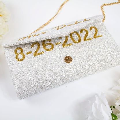 "Elegant custom envelope bridal clutch, meticulously beaded and handmade, showcasing intricate patterns. This 10" W x 6" H clutch with a gusset comes with a choice of gold or silver chain and an optional interior custom date. Perfect for carrying wedding essentials, each bridal clutch is a unique piece, highlighting the individual beauty of handmade crafts