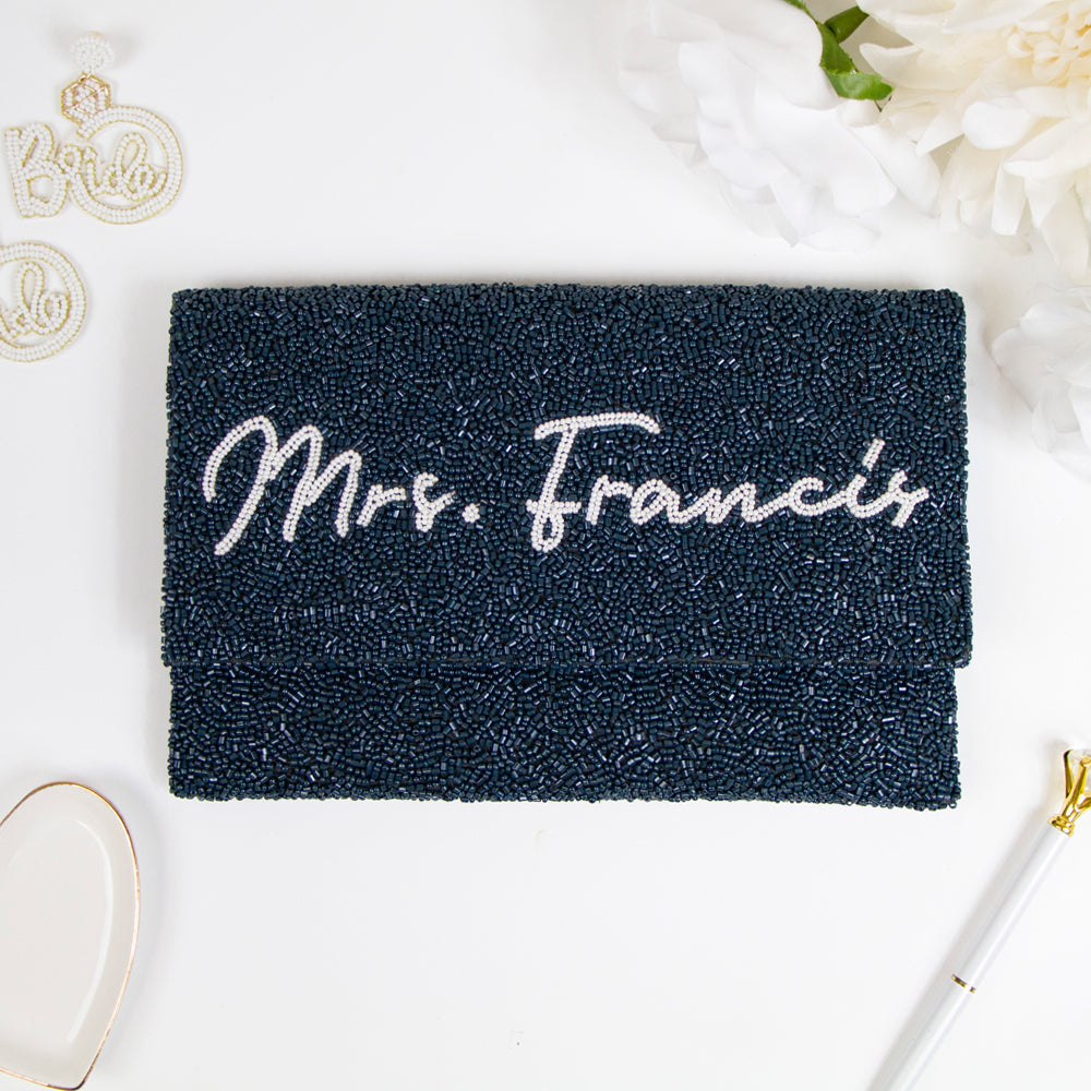 Exquisite Bridal Clutch: Custom Monogram Clutch Purse measuring 9 1/2″ wide x 5″ tall. Featuring rainbow clutch design with white text beading, complemented by a velvet interior. Each handmade clutch is unique, ideal for brides desiring a personalized touch on their special day