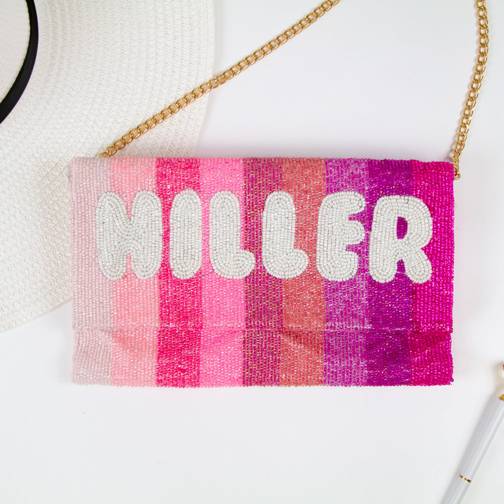 Exquisite Personalized Pink Ombre Clutch Bag, masterfully handcrafted for wedding occasions. Measuring 9.5 inches in length and 6 inches in breadth, this clutch features a gradient of pink hues, accented with white text beading. Complete with a gold or silver chain and plush velvet interior, it can be personalized with a date inside. A perfect blend of elegance and functionality, it's a distinctive accessory that adds a touch of sophistication to bridal attire.