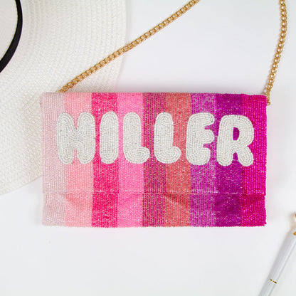 Exquisite Personalized Pink Ombre Clutch Bag, masterfully handcrafted for wedding occasions. Measuring 9.5 inches in length and 6 inches in breadth, this clutch features a gradient of pink hues, accented with white text beading. Complete with a gold or silver chain and plush velvet interior, it can be personalized with a date inside. A perfect blend of elegance and functionality, it's a distinctive accessory that adds a touch of sophistication to bridal attire.