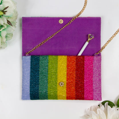 Elegant Custom Rainbow Clutch Purse, ideal for wedding occasions. Handcrafted with precision, this 9.5 inches wide by 5 inches tall clutch showcases a vibrant rainbow design complemented by white text beading. It boasts a soft velvet interior and can be adorned with a gold or silver chain. The option for a personalized date on the inside adds a unique touch, making it both a stylish and sentimental accessory for brides or as a heartfelt gift