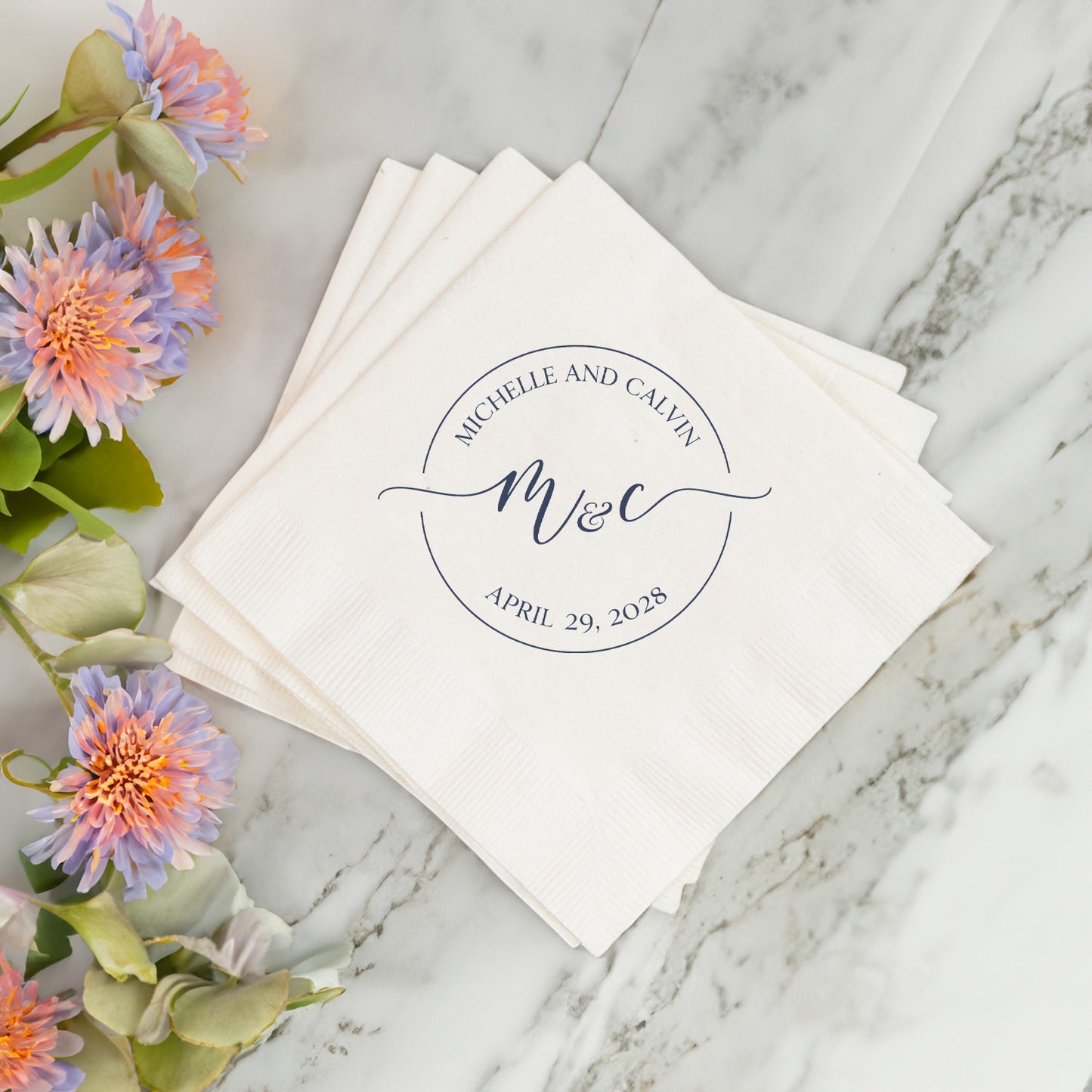 Stack of white napkins with personalized monogram and date on a marble surface with flowers.