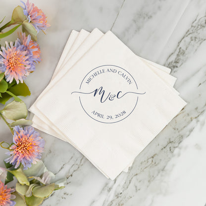Stack of white napkins with personalized monogram and date on a marble surface with flowers.