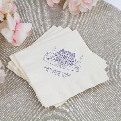Stack of white napkins with a blue logo and text on a textured surface with pink flowers.