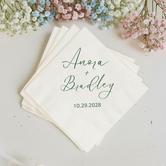Stack of personalized napkins with names and date, surrounded by small flowers on a light background