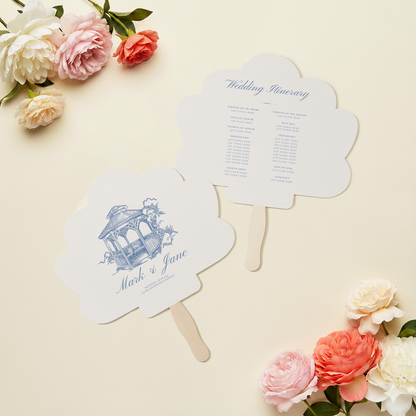 two white fan-shaped wedding programs with a blue and white design, placed on a light-colored background with pink and white flowers.