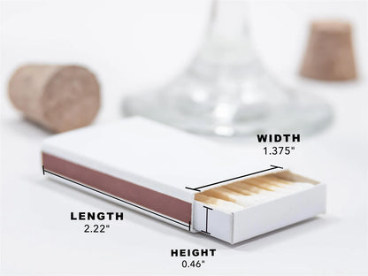 a matchbox with a cork stopper and a wine glass in the background. The matchbox is described as having a length of 2.22 inches, a height of 0.46 inches, and a width of 1.375 inches.