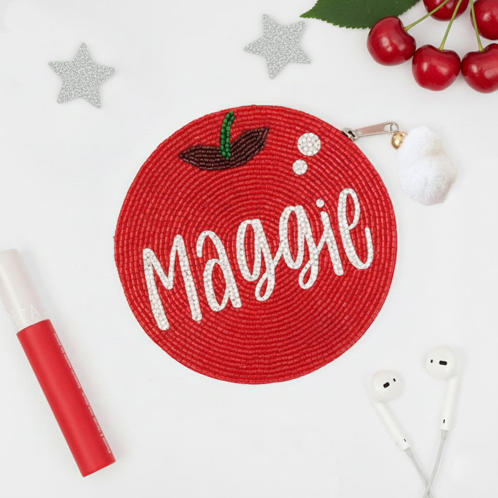a red circular object with the name "Magie" written on it, surrounded by various personal items such as a red marker, a pair of earphones, and some cherries.