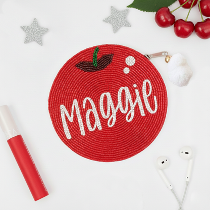 a red circular object with the name "Magie" written on it, surrounded by various personal items such as a red marker, a pair of earphones, and some cherries.