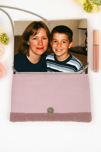 A pink handbag with a photo of a woman and a boy inside, along with some flowers and a tube of lip gloss.