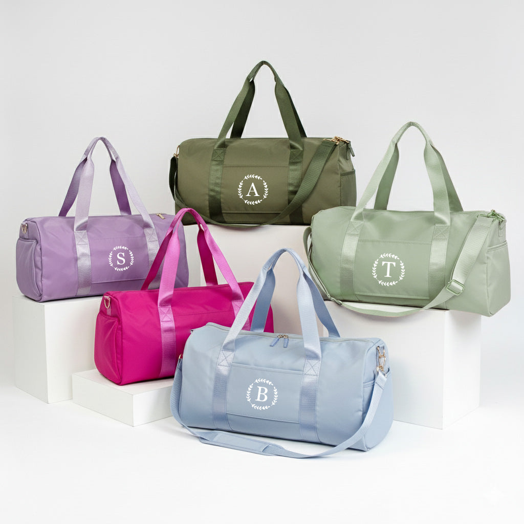 a collection of six colorful duffel bags, each with a unique monogram or logo, arranged on a white background.