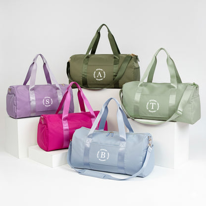 a collection of six colorful duffel bags, each with a unique monogram or logo, arranged on a white background.