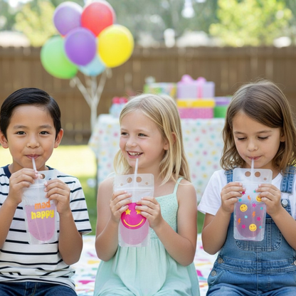 Three children are sitting together, each holding a drink from a clear plastic cup with a smiley face on it. In the background, there are colorful balloons and gift boxes, suggesting a festive occasion.