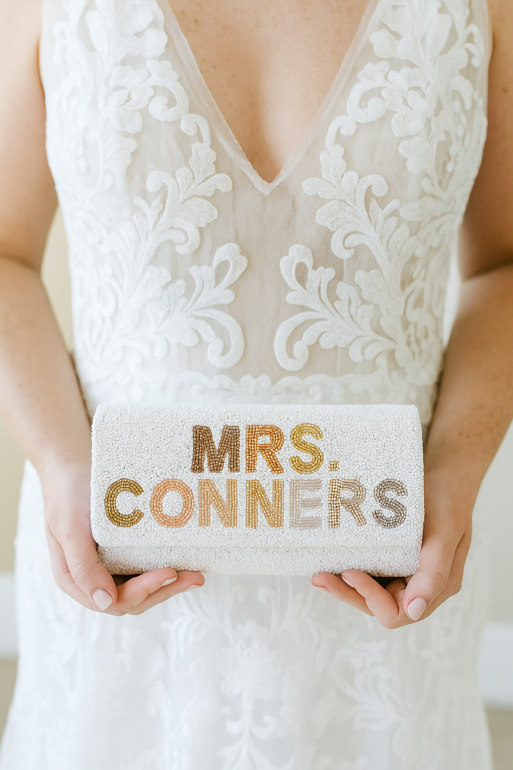 A person is holding a small white clutch purse with the text "MRS. CONNERS" printed on it.