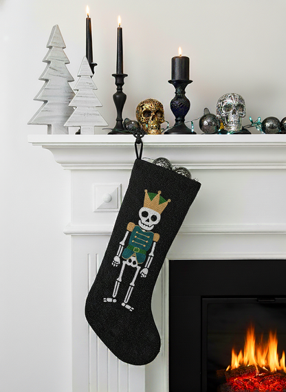A black stocking hanging on a white fireplace mantle, featuring a skeleton figure wearing a crown.