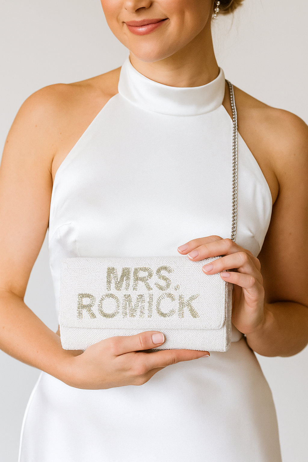 A woman in a white dress holds a small white clutch purse with the text "Mrs. Romick" printed on it.