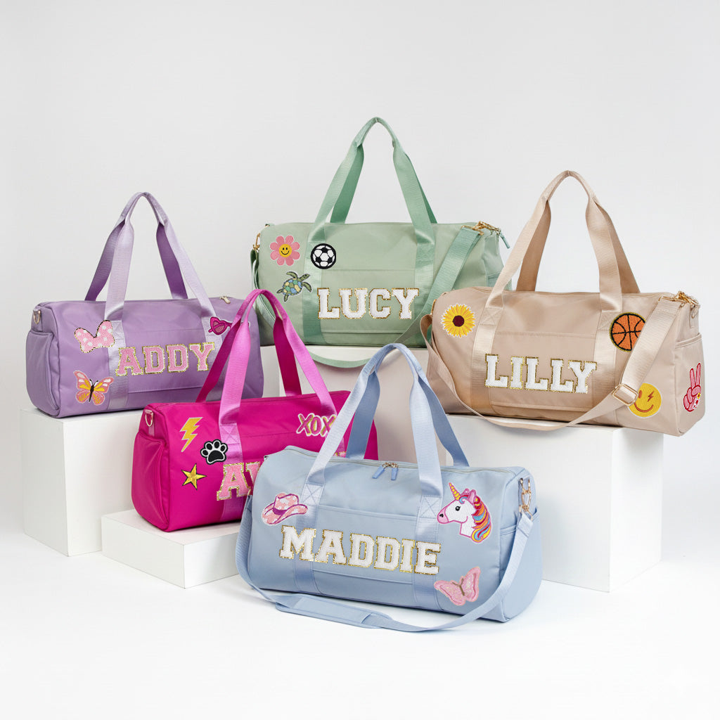 A collection of colorful duffle bags with personalized names on them, including "ADDY", "LUCY", "LILLY", "MADDIE", and "XOX".