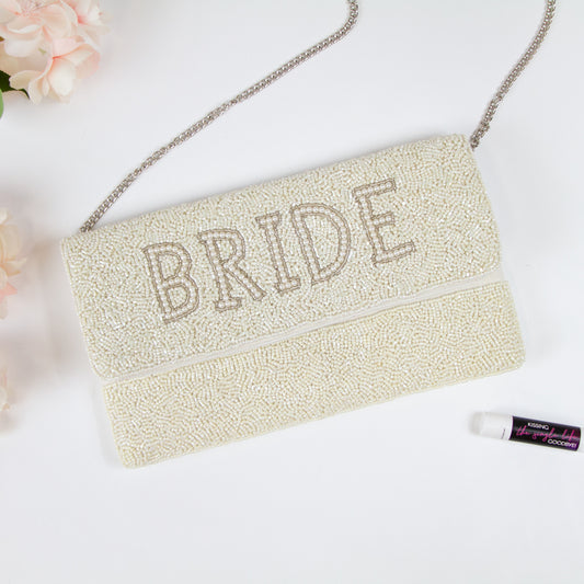 Elegant Bridal Clutch: White Bride Clutch Purse with gold text, measuring 10.5 x 6 x 1 in. Crafted from durable canvas with a magnetic snap closure. Each clutch is handmade, showcasing intricate beading patterns, ensuring a unique and special accessory for the bride on her big day