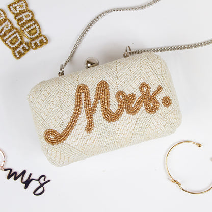 Elegantly handcrafted Bride, Mrs. Bridal Clutch in white with intricate gold text and beading. Perfect for a wedding day, this unique bridal clutch seamlessly blends functionality and style, holding all essentials with grace. A one-of-a-kind gift option for brides, showcasing the distinct beauty of artisanal craftsmanship.