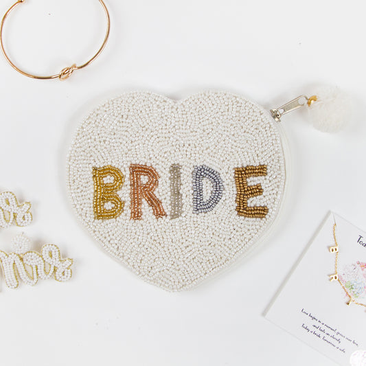 Bride Coin PurseElegant Bride Coin Purse featuring intricate hand-beaded design. This bridal clutch, made of durable canvas, presents a beautiful contrast of matte white beading and gold shine. Perfect for weddings, it offers a secure zipper to keep belongings safe. Measuring compactly, it's both stylish and functional, allowing brides to carry their essentials with grace. Each purse is uniquely crafted, ensuring a one-of-a-kind accessory for any special occasion